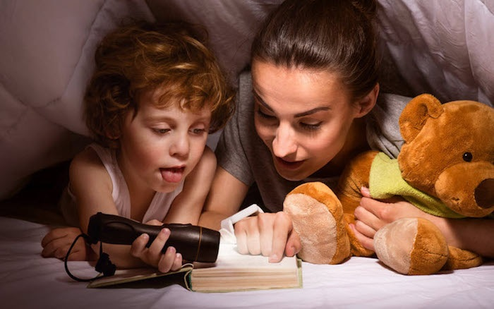 babysitter and child under blanket reading with a flashlight