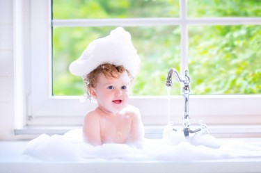 Funny baby girl playing with water and foam in a big kitchen sin
