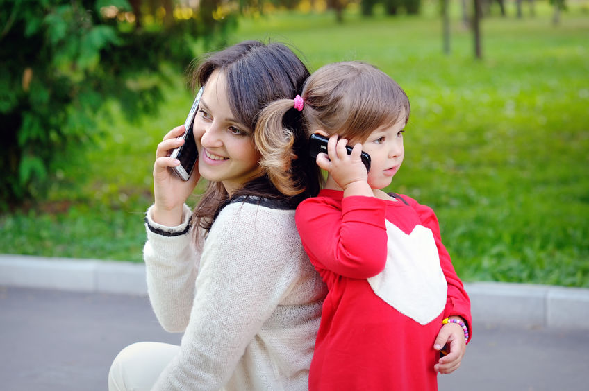 mother, daughter, toddler, cell phone, talking, red, brunette, pink, sweater, grass, green, pavement