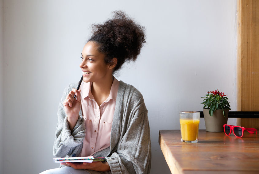 woman, journal, pen, shirt, sweater, cardigan, table, juice, sunglasses, plant, wood, red, orange, pink, grey