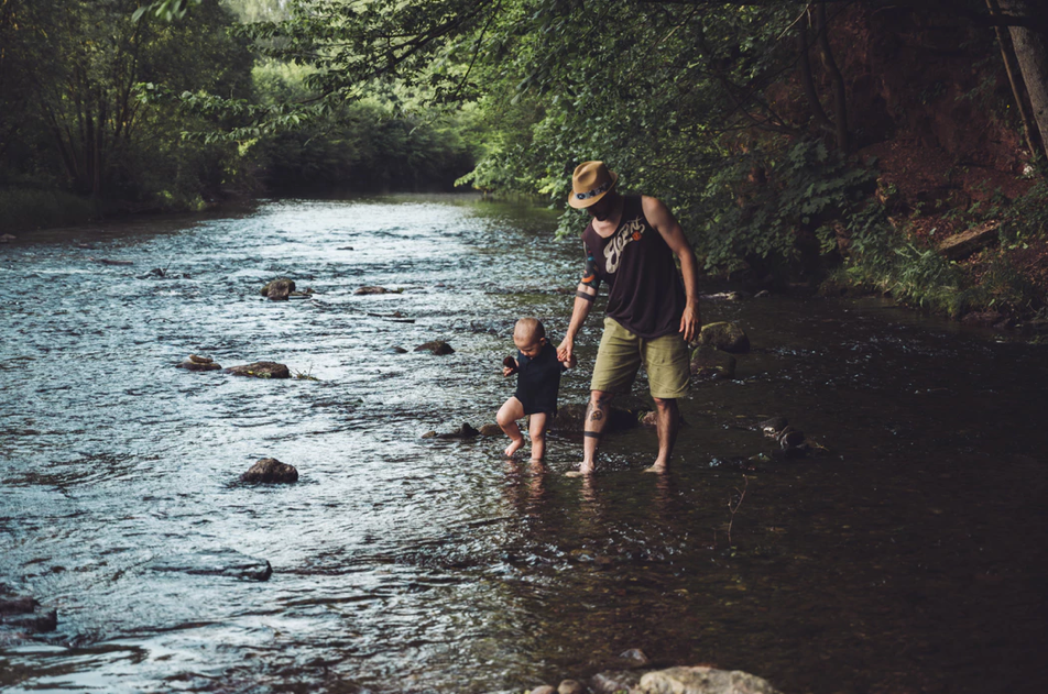man, father, child, son, river, rocks, trees, green, blue, forest, outdoors, hat, tan, shorts, onesie
