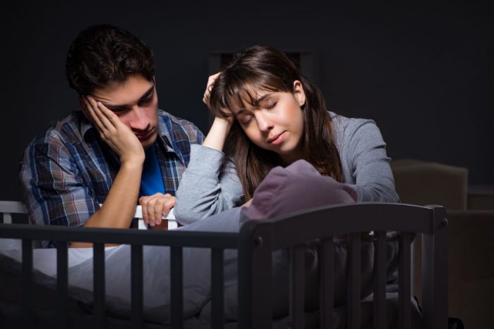 exhausted couple sitting with newborn baby