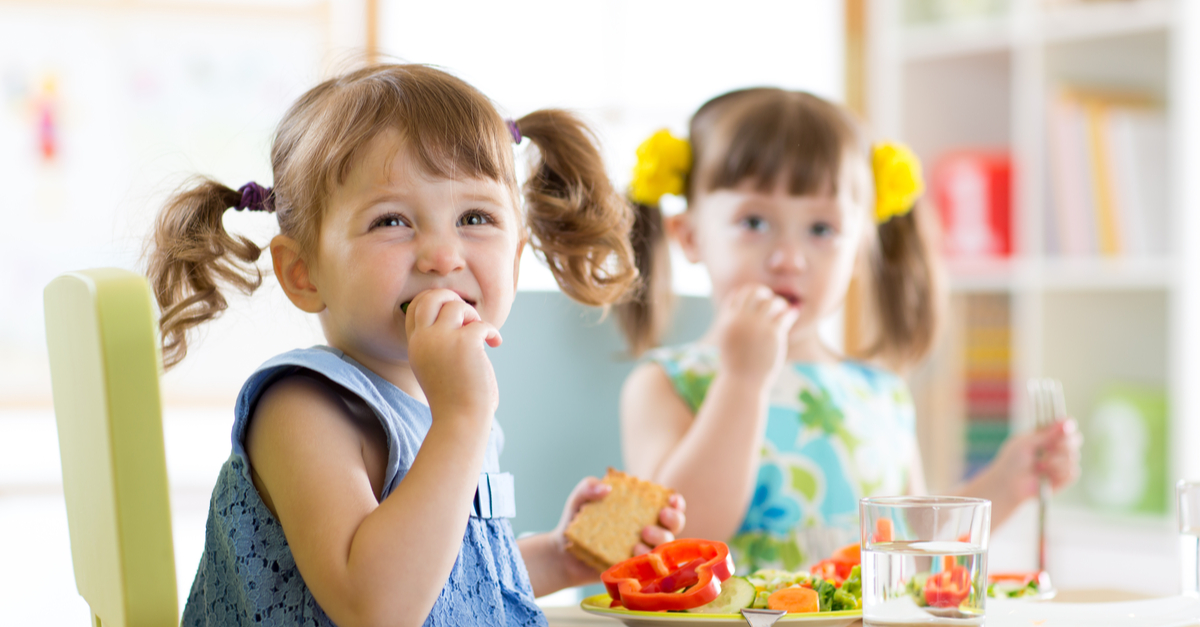 two young school girls eating healthy, nutrious vegetable snack