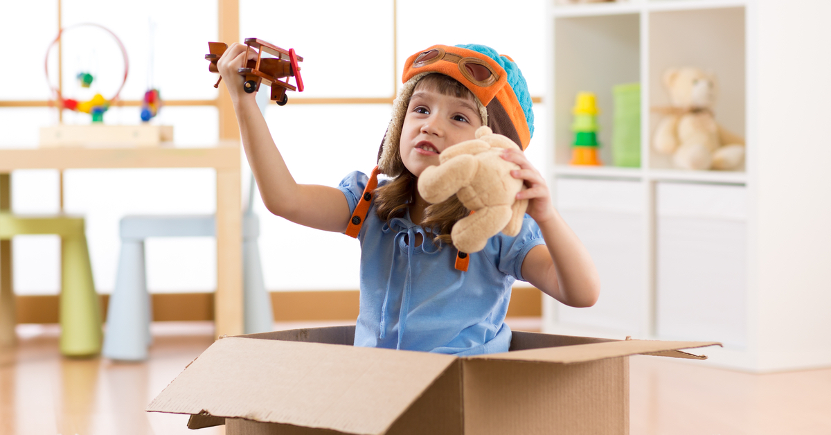 girl sitting in cardboard box playing with toy airplane