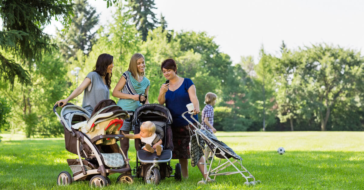 moms with babies and strollers reading a text message in a park