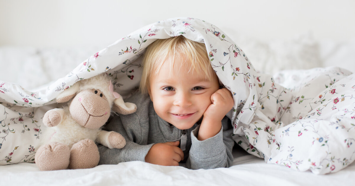 toddler with stuffed animal under comforter