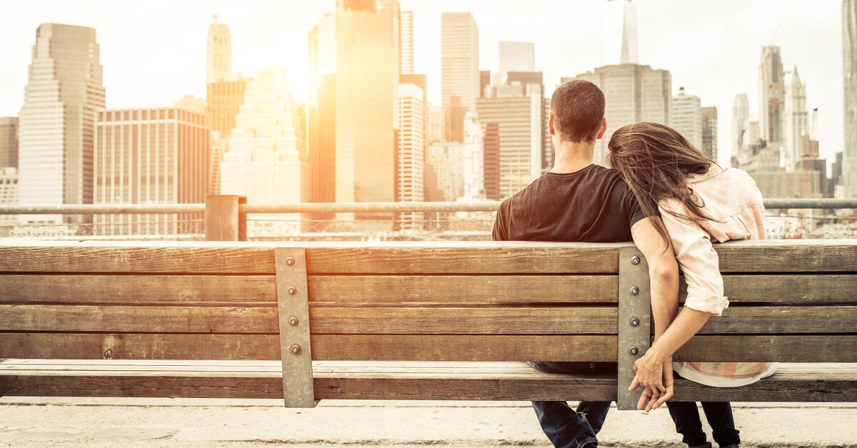 a couple sitting on a bench looking out at the NY skyline