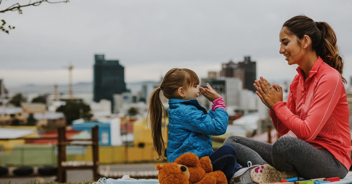 nanny playing hand game outside with girl
